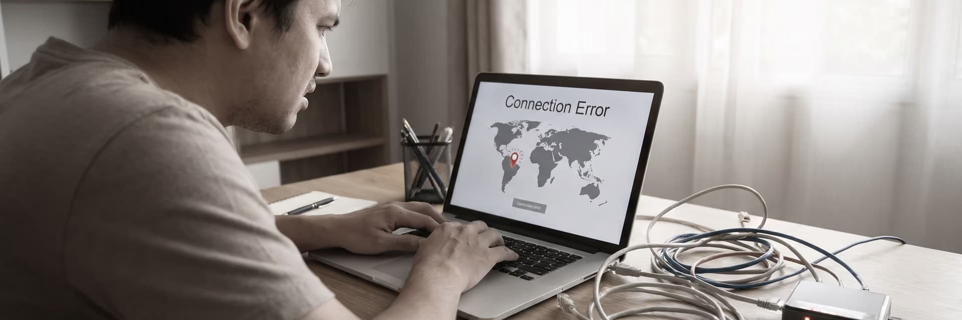 Мужчина сидит за столом с ноутбуком, на экране которого сообщение об ошибке подключения.
